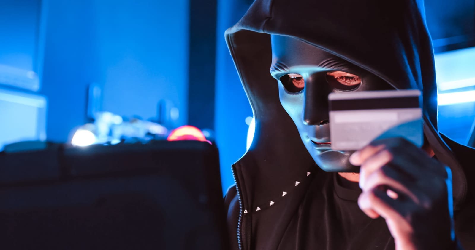 Person in mask steals credit card information in front of computer
